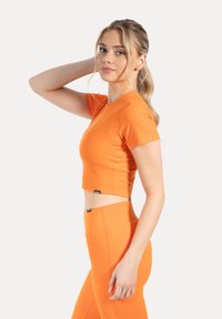 Haut athlétique court orange à manches courtes, texture lisse et coupe ajustée, assorti à un legging taille haute assorti.