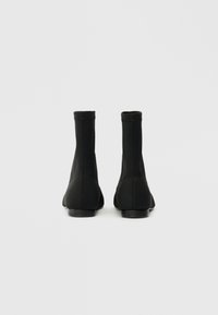 Crne gležnjače s elegantnim, prilagođenim dizajnom. Izrađene od glatkog materijala, s zaobljenim vrhom i niskom petom. Minimalistički detalji šivanja.
