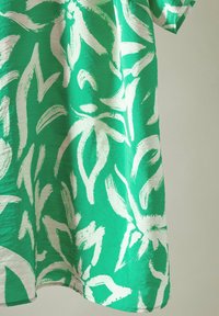 Vestido verde de manga corta con grandes patrones florales en blanco, que presenta una tela ligera y ligeramente texturizada con un corte holgado.