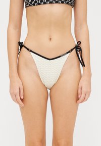 Bež bikini dno s strukturiranim, tkanim dizajnom. Ima črne zaveze ob strane in kontrastni črni pas.
