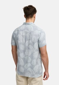 Camisa de manga corta en azul claro, con un patrón de hojas de palma blancas, la textura de la tela parece suave, con un cuello abotonado y un detalle en el yugo trasero.