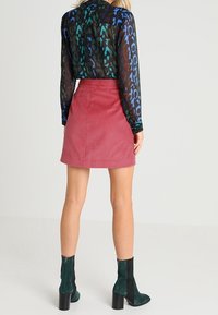 Blusa nera leggera e trasparente con stampa leopardata vibrante in blu, verde e marrone, abbinata a una mini gonna in corduroy rosa e stivali con tacco blocco neri e verdi.