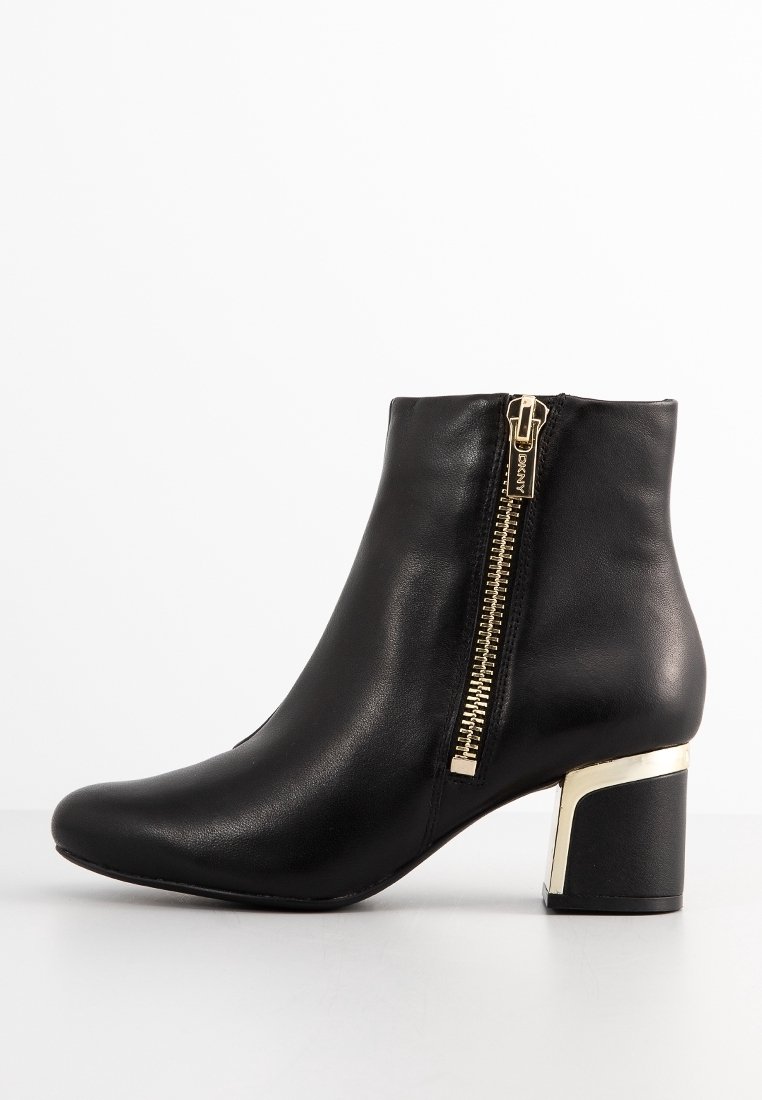 Bottine noire en cuir avec un bout arrondi, une fermeture éclair dorée, et un accent métallique doré sur le talon bloc. Texture lisse.