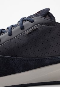 Sneaker in pelle blu scuro con design perforato, lacci blu navy, accenti in suede e suola beige con dettagli logo discreti.
