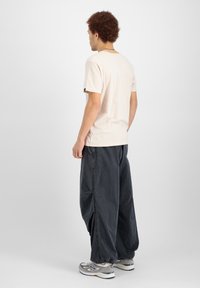 Světle béžové bavlněné tričko s krátkými rukávy a kulatým výstřihem, ve spojení s tmavě šedými oversized kalhotami a šedými sportovními botami.