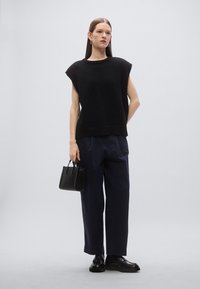 Zwart gebreid mouwloos topje, marineblauwe broek met brede pijpen, klein zwart handtasje en zwarte loafers. Simpel ontwerp met een losse pasvorm.