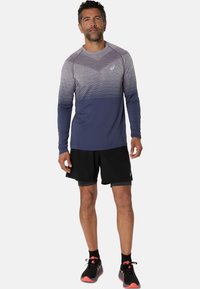 Långärmad sporttopp i gradient grå och marinblå färger, med rund halsringning och strukturerad design, tillsammans med svarta shorts och löparskor.