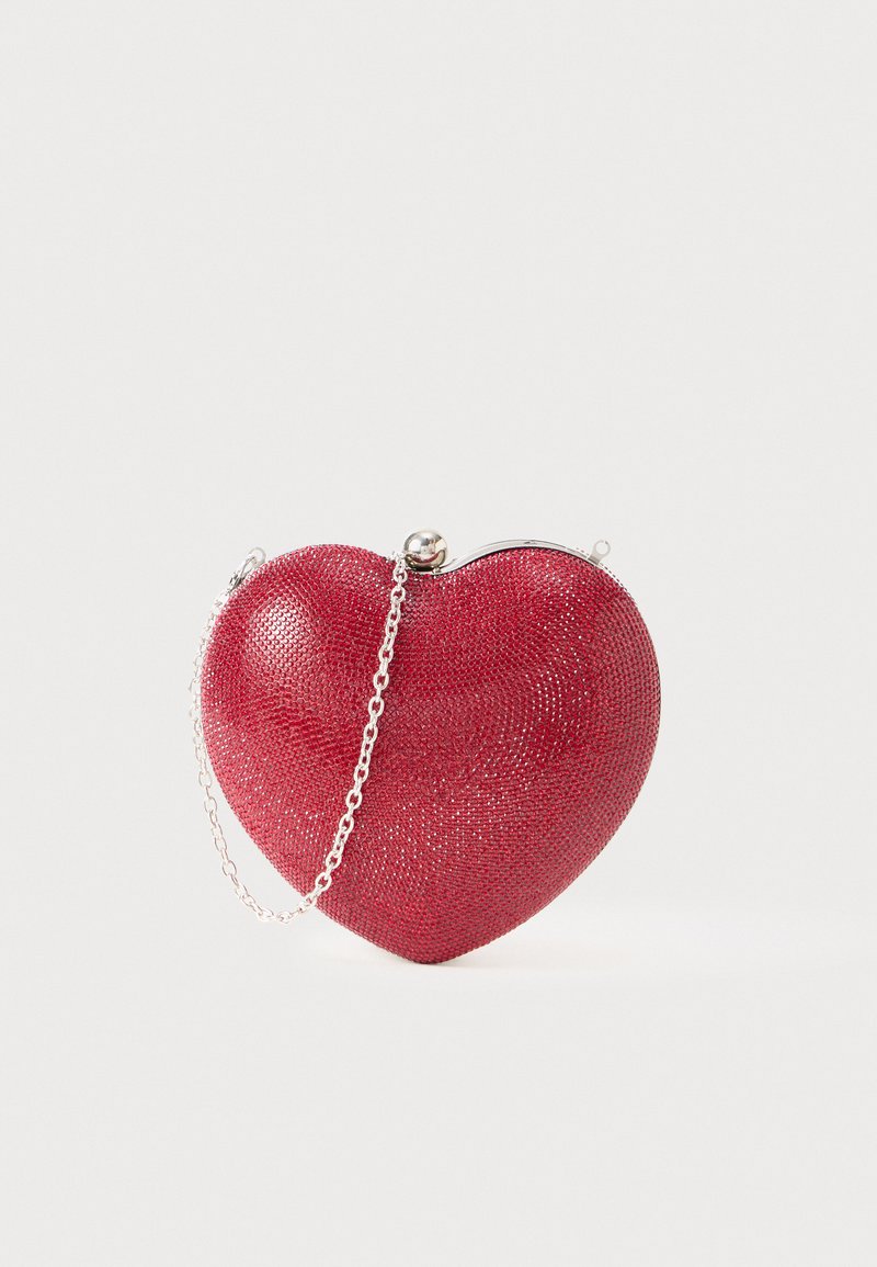 Rdeča torbica v obliki srca, izdelana iz teksturiranega materiala, z srebrno verižico in dekorativnim zapiralom na vrhu.