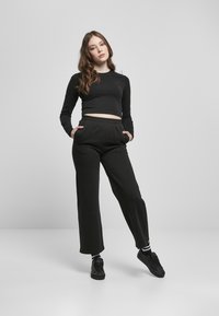 Zwarte cropped lange mouwen top gecombineerd met zwarte broek met elastische taille. De outfit heeft een losse pasvorm en wordt compleet gemaakt met zwarte sneakers.