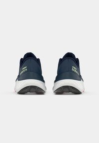 Blauwe sportschoenen met een gestructureerde bovenkant, voorzien van een witte, gevoerde zool en subtiele roze accenten. "new balance" logo in lichtgroen.
