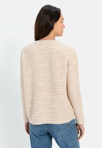 Beige gestrickter Pullover mit strukturiertem Streifenmuster, rundem Halsausschnitt und langen Ärmeln, getragen über blauen Jeans. Rückansicht dargestellt.