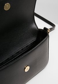 Borsa a tracolla in pelle nera con finitura testurizzata, hardware dorato e chiusura a scatto. L'interno è foderato in tessuto con scomparti.