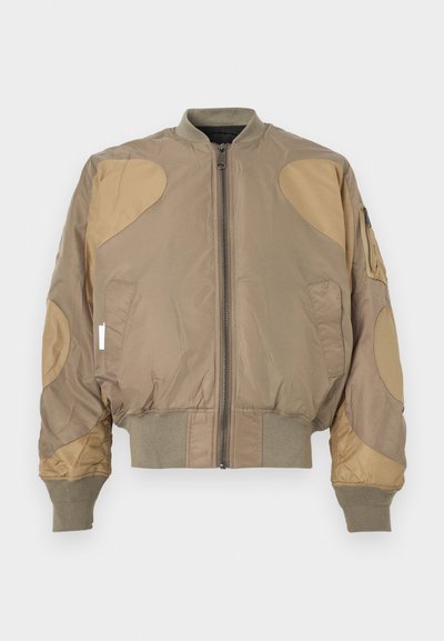 Μπουφάν bomber σε χακί χρώμα με αντίθετα μπεζ patches, φερμουάρ μπροστά, πλεκτά μανσέτες και μέση, με πλαϊνές τσέπες και τσέπη στον ώμο.