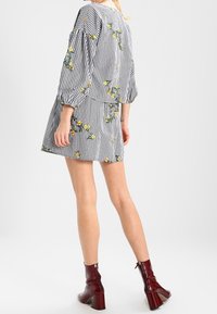 Schwarz-weißer kariert Mini-Kleid mit Puffärmeln, verziert mit gelber Blumenstickerei und rundem Ausschnitt, kombiniert mit burgunderfarbenen Stiefeletten mit Absatz.