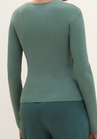 Prążkowany top z długim rękawem w stonowanym zielonym kolorze. Dopasowana sylwetka z okrągłym dekoltem i teksturowaną tkaniną. Gładkie wykończenie ze streczem dla komfortu.