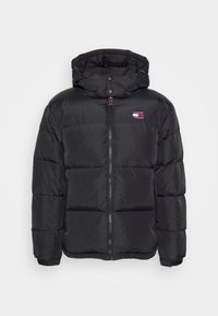 Schwarze Pufferjacke mit Kapuze, ausgestattet mit einem Frontreißverschluss, Druckknöpfen und einem kleinen Logopatch auf der linken Brust. Glatte Textur.