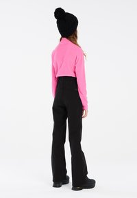 Ružový skrátený fleece top, vysoké čierne nohavice s hladkou textúrou a čierne masívne topánky s žltými akcentmi. Čierna čiapka s brmbolcom.