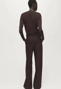 Pulover maro de tricot cu mâneci lungi, asortat cu pantaloni maro cu talie înaltă și croială largă; textură moale, design minimal, fără modele vizibile.