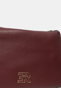 Borsa a tracolla in pelle bordeaux con una finitura testurizzata, caratterizzata da un accento del logo dorato e una chiusura a zip nella parte superiore.