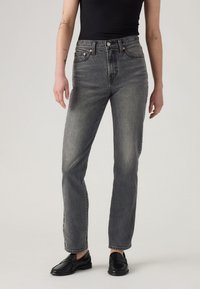 Sive visoke kavbojke s ravnim krojem, z bledejšim pranjem, petimi žepi in kovinskimi okraski. Brez vidnih vzorcev.