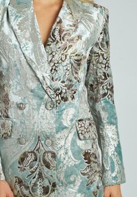 Blazer in velluto di un delicato color turchese, caratterizzato da intricate fantasie floreali in marrone e verde, design doppiopetto con bottoni argentati e tasche.