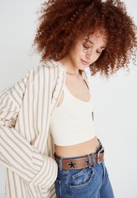 Camicia a righe beige e bianca indossata sopra una canotta a coste color crema, abbinata a jeans blu e una cintura marrone con accenti a forma di stella.
