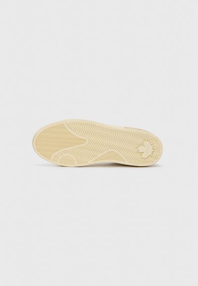 Kermanvärinen tennarin pohja, jossa on kuviollinen herringbone-malli ja pyöreä logo-yksityiskohta. Silkkisen sileä pinta, jossa on hieno kiilto tietyissä kohdissa.