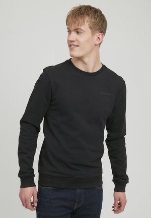 Svart sweatshirt laget av bomullsblanding, med rund hals, lange ermer, ribbestrikkede mansjetter og en liten logo på brystet. Ledig passform.