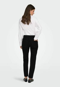 Pantalones de mezclilla negros con cintura alta, corte recto y dos bolsillos traseros. Combinados con una camisa blanca de botones y zapatos negros con tachuelas.