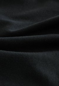 Detailní záběr na měkkou černou látku s jemnou tkanou strukturou a mírnými záhyby vytvářejícími jemné stíny.