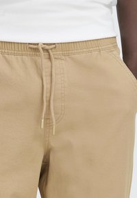 Khaki jogger pants featuring an elastic waistband with a drawstring, made of soft fabric with a smooth texture and subtle stitching details.