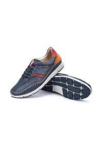 Sneaker in pelle blu con design perforato, accenti rossi e arancioni a contrasto, suola bianca maculata e cuciture visibili lungo i bordi.
