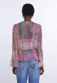 Blusa a maniche lunghe trasparente e multicolore con intricate fantasie paisley e vestibilità ampia, abbinata a jeans in denim blu a vita alta.