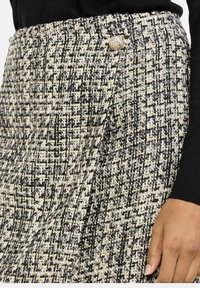 Čierna a krémová tweedová sukňa s textúrovaným povrchom, s zlatým gombíkom na páse. Strih zdôrazňuje štruktúrovaný dizajn.