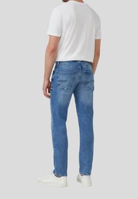 Blaue Jeans im Slim-Fit-Schnitt, mit Gesäßtaschen und einem subtilen Verblassen. Kombiniert mit einem weißen T-Shirt und weißen Sneakers.