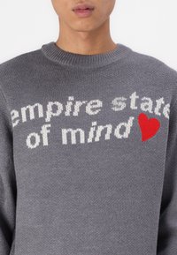Szary sweter z dzianiny z napisem "empire state of mind" na białym tle oraz czerwonym sercem na rękawie. Design z okrągłym dekoltem.