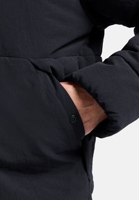 Giacca puffer blu navy con finitura testurizzata, dotata di una tasca laterale e chiusura a bottoni a pressione sui polsini.