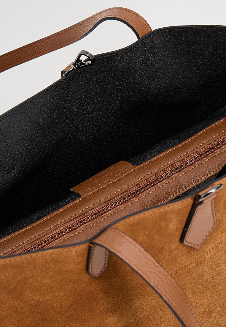 Braune Wildleder-Tasche mit schwarzem Futter, ausgestattet mit einer Reißverschlusstasche und zwei Ledergriffen zum Tragen. Mit sichtbaren Steppnähten.