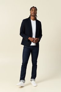 Marinblå blazer med strukturerade axlar, kombinerad med en vit t-shirt och mörk denimjeans, avslutad med vita sneakers. Enkel, avslappnad design.