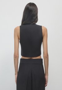 Top nero senza maniche e corto con una texture liscia e un collo alto. Il retro presenta un pulito dettaglio di cucitura e una silhouette aderente.