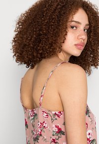 Vestido com estampa floral, fundo rosa, alças finas e design costas abertas. Apresenta flores vermelhas e brancas, tecido leve e um ajuste descontraído.