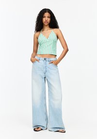 Groen en wit gestreepte crop top met een V-hals ontwerp en halterbandjes, gecombineerd met lichtblauwe wijde jeans en zwarte sandalen.