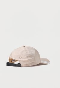 Bežna kapa s zakrivljenim vizirjem, izdelana iz lahkega materiala. Ima dve beli črti na vizirju in nastavljiv črn trak na zadnji strani.