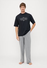 Camiseta negra de manga corta con gráfico "VIBES" en blanco, combinada con pantalones de lounge ligeros en gris. Mezcla de algodón suave, corte holgado.