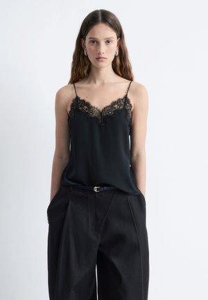 Black camisole with delicate lace trim at the neckline, featuring thin straps. Paired with high-waisted black trousers and a slim belt.