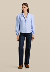 Blauw-wit gestreepte button-up shirt met een kraag, lange poffende mouwen en een ontspannen pasvorm, gecombineerd met donkerdenim jeans en bruine enkellaarzen.