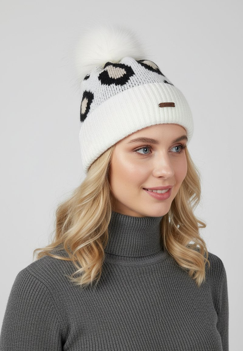 White knitted beanie with black and beige leopard print, featuring a fluffy pom-pom on top and a branded metal accent on the cuff.