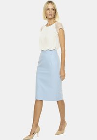 Biała bluzka z przezroczystymi, kropkowanymi rękawami, zestawiona z jasnoniebieską spódnicą o ołówkowym kroju, charakteryzującą się gładką fakturą i małym srebrnym akcentem.