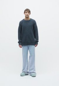 Gray textured knit sweater, light blue wide-leg pants, and green clogs. Simple design with a relaxed fit, minimalistic and monochromatic colors.