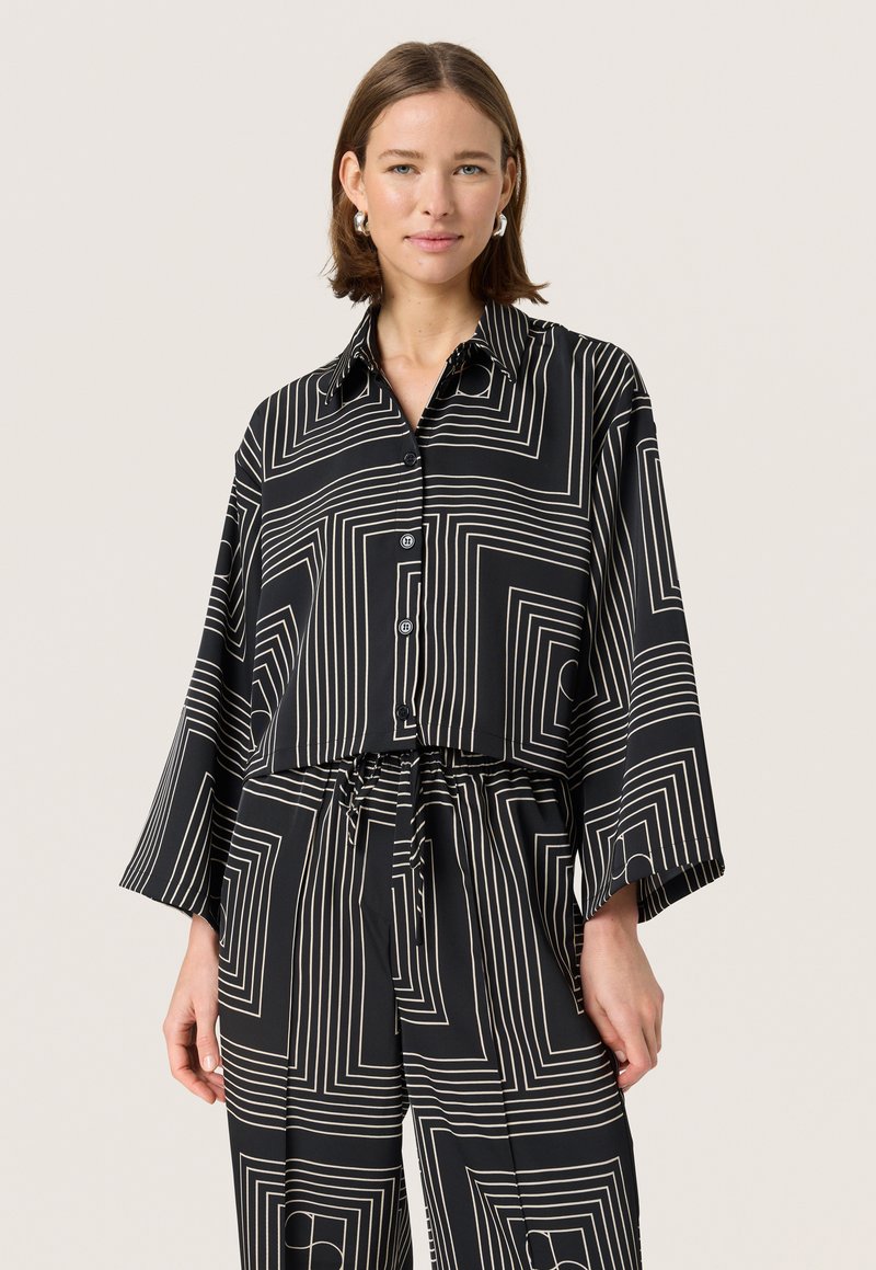 Cămașă neagră scurtă cu un model geometric alb, cu mâneci lungi, guler și nasturi în față. Asortată cu pantaloni cu model similar.